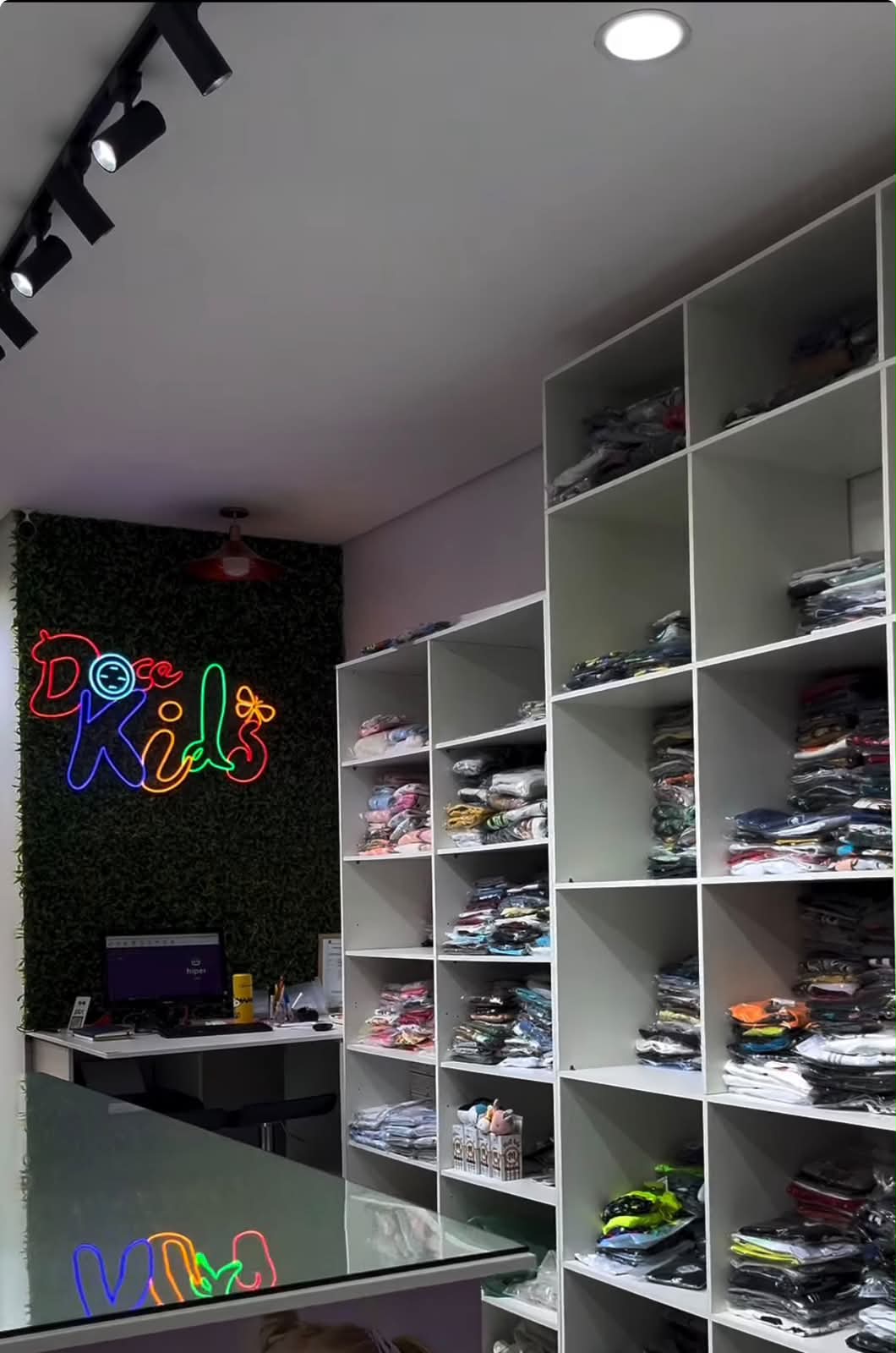 Letreiro neon da Doce Kids na parede verde decorada da loja